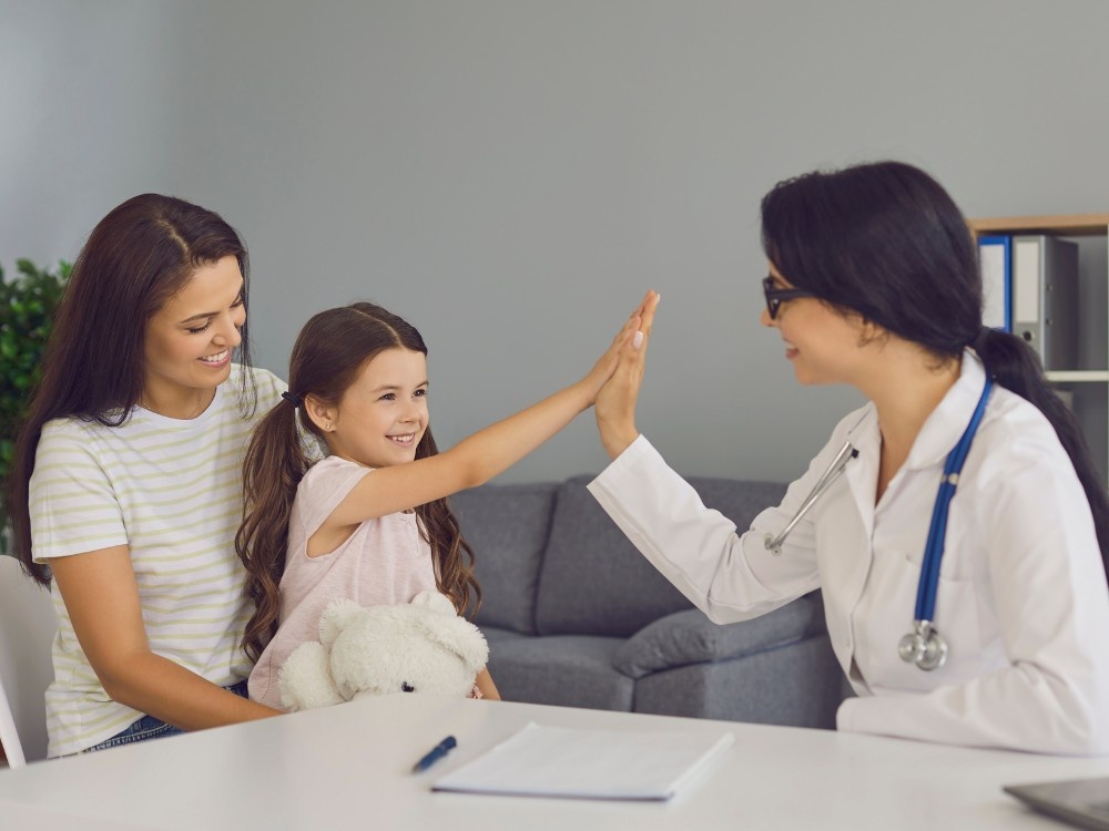 A friendly doctor giving a high-five to a young girl during a visit to an allergy testing and treatment clinic.